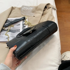 Detail of black crocodile texture leather handbag with gold chain strap on a bed