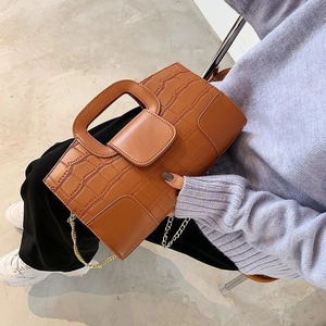 Detail of brown crocodile pattern handbag with golden chain strap and top handle