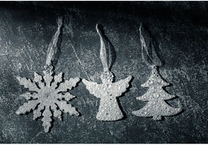 Nahaufnahme glitzernder Acryl-Ornamente in Schneeflocken- und Engelform auf grauem Grund