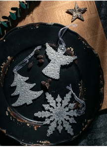 Makroaufnahme von glitzernden Acryl-Schneeflocken und Engel-Anhängern auf dunklem Teller