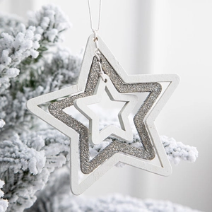 White wooden star ornament with silver glitter hanging on a snowy Christmas tree