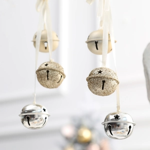 Glittery gold and silver Christmas bell ornaments hanging with white satin ribbons