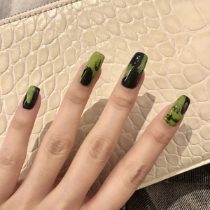 Faux ongles longs carrés avec design graffiti noir et vert présentés sur une main élégante