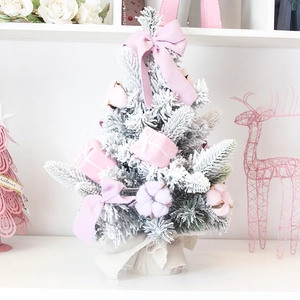 Pink flocked mini Christmas tree with snow effect and ribbon on white minimal stand
