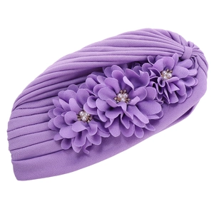 Gros plan détaillé du turban plissé violet avec trois fleurs en tissu et strass brillants