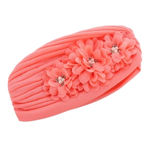 Détail d'un turban plissé corail pour bébé avec trois fleurs en mousseline et strass