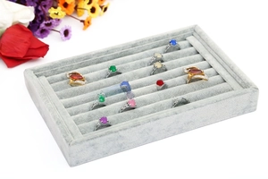 Gray velvet jewelry tray with multiple slots displaying colorful gemstone rings closeup