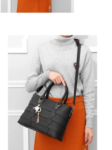 Detail of black woven PU leather handbag with gold cat charm and tassel on model