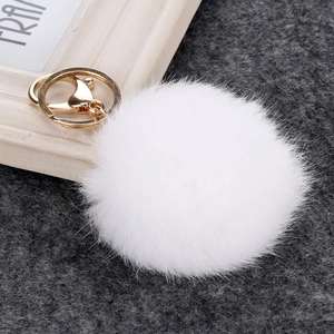 Close-up of white fluffy faux rabbit fur pom pom with golden metal keychain and lobster clasp