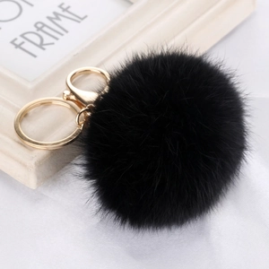 Detail of fluffy black faux fur pompom with golden metal lobster clasp and keychain