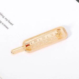 Détail d'une broche thermomètre dorée avec échelles gravées sur fond de page de livre