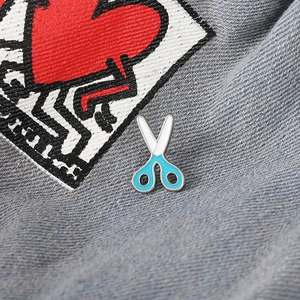 Detailed close-up of blue and white enamel scissor brooch pinned on denim fabric jacket