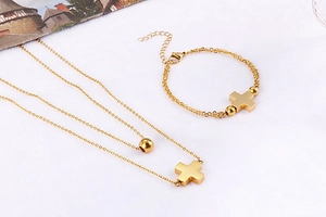 Detail of gold double-layer cross necklace and matching bead bracelet on white surface