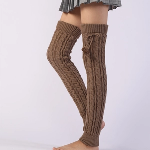 Detail view of cable knit leg warmers in warm brown with pom-pom ties over the knee