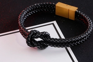 Detailed view of black braided leather bracelet with golden clasp on white card