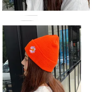 Detail of bright orange knitted beanie with white daisy embroidery and thick texture
