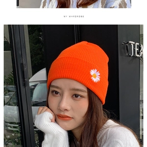 Detail of orange knit beanie with white daisy embroidery and ribbed texture on model