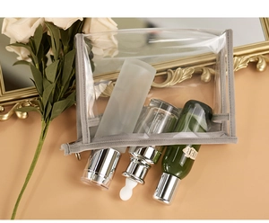 Elegant clear cosmetic bag with grey trim displayed near a vintage gold frame and white roses