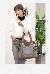 Detail of grey canvas tote bag featuring brown woven handles and adjustable shoulder strap