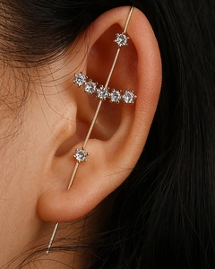 Macro shot of gold ear climber with inlaid crystals on an earlobe over dark hair
