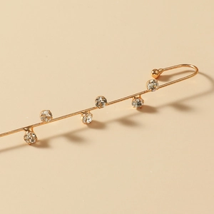 Close-up of golden rhinestone ear crawler with six sparkling crystals on beige background