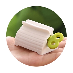 Manual rolling tube toothpaste squeezer in green and white shown held in a hand