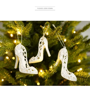 Three white glitter high heel ornaments hanging on a Christmas tree with warm LED lights