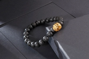 Gros plan sur les perles de lave noire et le charm tête de mort doré du bracelet