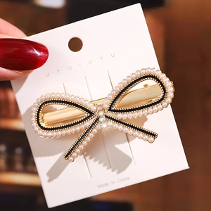 Detail of a golden bow hair clip with white pearls and a sparkling center rhinestone