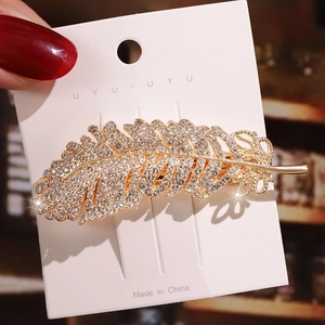 Close-up of golden feather hair clip with sparkling rhinestones on display card