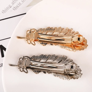 Detailed close-up of golden and silver feather-shaped alloy hair clips on a white plate