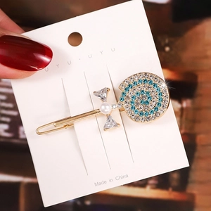 Close-up of golden lollipop hair clip with blue rhinestones and pearl bow detail