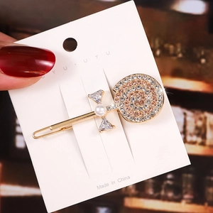 Detail of a gold lollipop-shaped hair clip with inlaid rhinestones and a small pearl bow