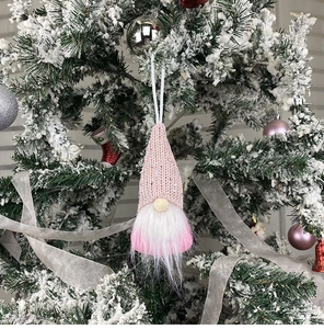 Pink and white handmade Christmas gnome ornaments hanging on a snowy Christmas tree branch