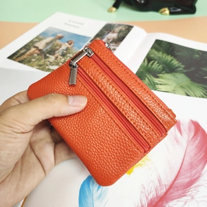 Detail of orange textured leather coin purse with double zippers held over a book