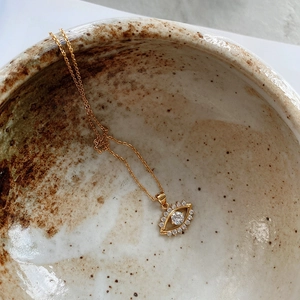 Detailed shot of gold evil eye pendant with pavé cubic zirconia in a ceramic bowl
