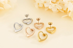 Three pairs of heart stud earrings in silver, rose gold, and gold on a beige surface