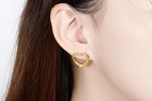 Close-up of model wearing gold hollow heart-shaped earrings in polished stainless steel