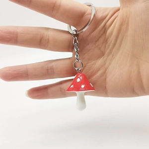 Close-up of a red mushroom keychain with white spots held in hand on white background