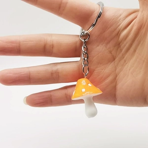 Close-up of a cute orange resin mushroom keychain with white spots held in hand