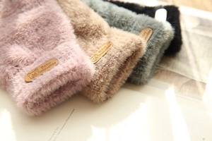 Close-up of four plush winter gloves in pink, beige, green, and black with bear tags