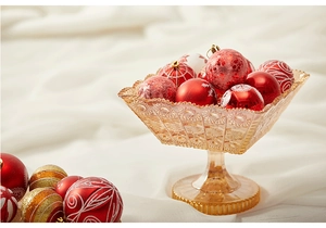 Detail of red and gold Christmas ornaments in an amber glass fruit bowl on silk
