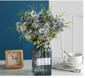 Blue and purple artificial daisies in a striped glass vase on a white table