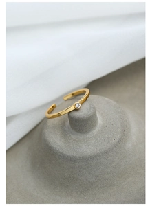Dettaglio anello regolabile placcato oro con zircone rotondo su un supporto minimalista