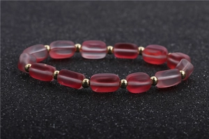 Detailed view of red frosted cylindrical beads and gold metal spacers on this bracelet