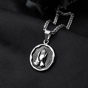 Titanium steel praying hands necklace with silver round pendant on dark fabric