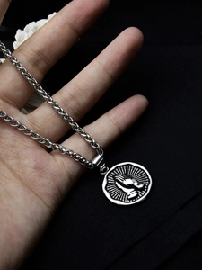 Macro shot of silver praying hands circular pendant on a stainless steel necklace