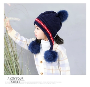 Detail of navy knit kids winter hat with faux fur pom-poms and fleece ear flaps
