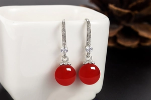Detail view of silver drop earrings with red agate beads and zircon accents on a white cup