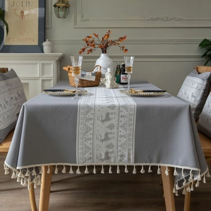 Green Christmas tablecloth with white reindeer pattern and fringe in cozy dining room